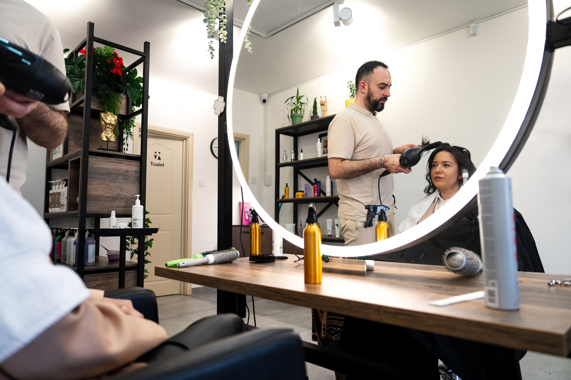 Male hairdresser using blow dryer to style female client’s hair